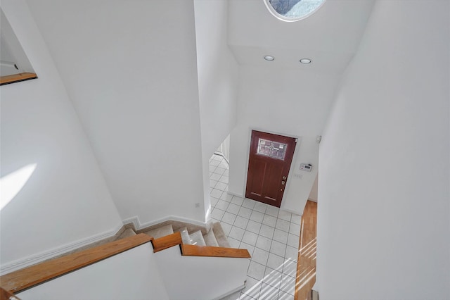 foyer entrance with stairs, a towering ceiling, baseboards, and light tile patterned floors