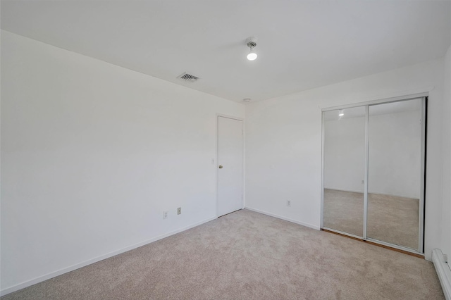 unfurnished bedroom with baseboards, visible vents, carpet, a baseboard heating unit, and a closet