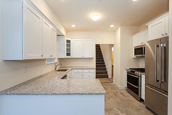 kitchen featuring kitchen peninsula, sink, stainless steel appliances, white cabinets, and light stone counters