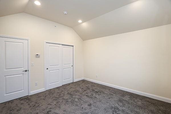 unfurnished bedroom with vaulted ceiling, a closet, and dark carpet