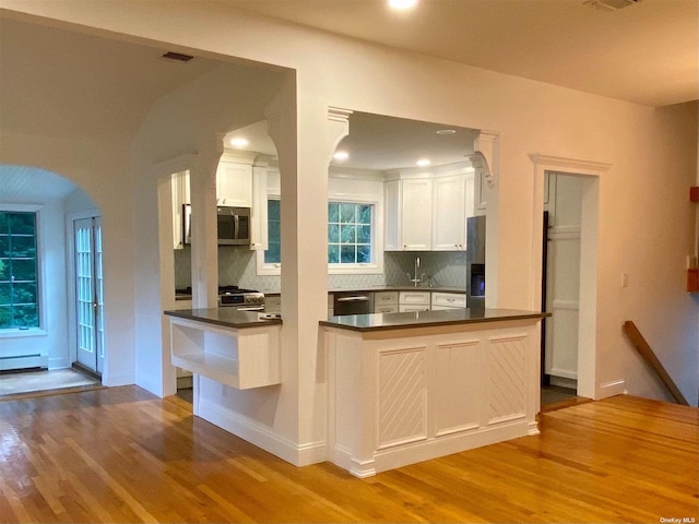 kitchen featuring stainless steel appliances, white cabinetry, kitchen peninsula, light hardwood / wood-style flooring, and decorative backsplash