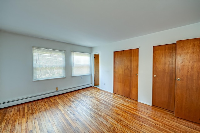 unfurnished bedroom with a baseboard radiator, light hardwood / wood-style floors, and multiple closets