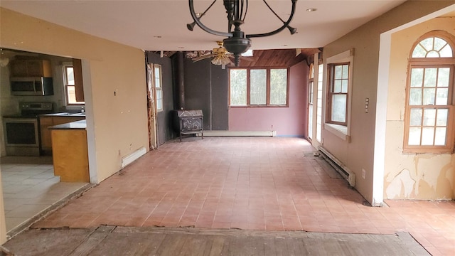 unfurnished dining area with ceiling fan, a wealth of natural light, a wood stove, and a baseboard radiator