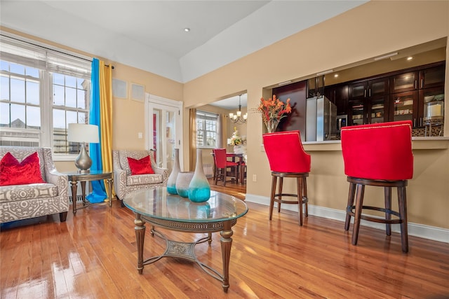 living area with hardwood / wood-style flooring, vaulted ceiling, and an inviting chandelier