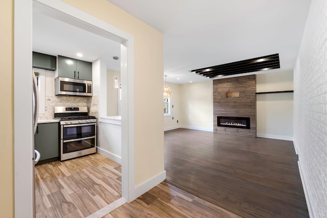 kitchen with decorative backsplash, light hardwood / wood-style flooring, stainless steel appliances, and a fireplace