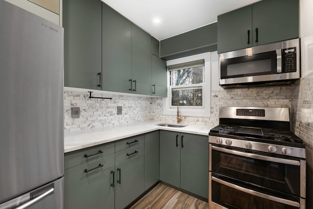 kitchen with light wood-type flooring, decorative backsplash, appliances with stainless steel finishes, and sink