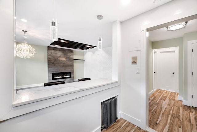 kitchen featuring decorative light fixtures, a fireplace, radiator, light wood-type flooring, and light stone countertops