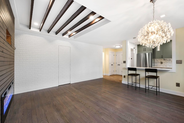 unfurnished living room with beam ceiling, a notable chandelier, brick wall, and dark hardwood / wood-style floors