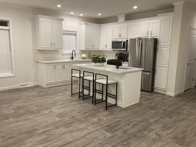 kitchen with a kitchen bar, sink, a kitchen island with sink, stainless steel appliances, and white cabinets