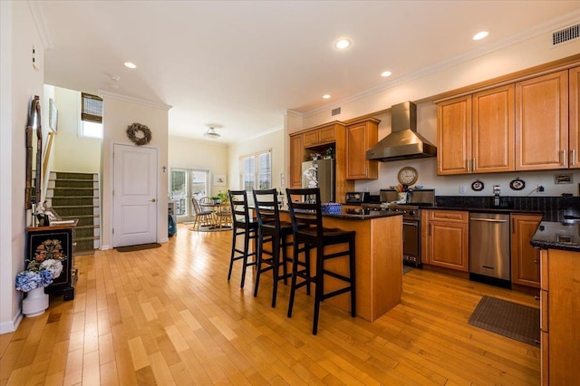 kitchen featuring light hardwood / wood-style floors, a breakfast bar area, stainless steel appliances, a kitchen island, and wall chimney exhaust hood