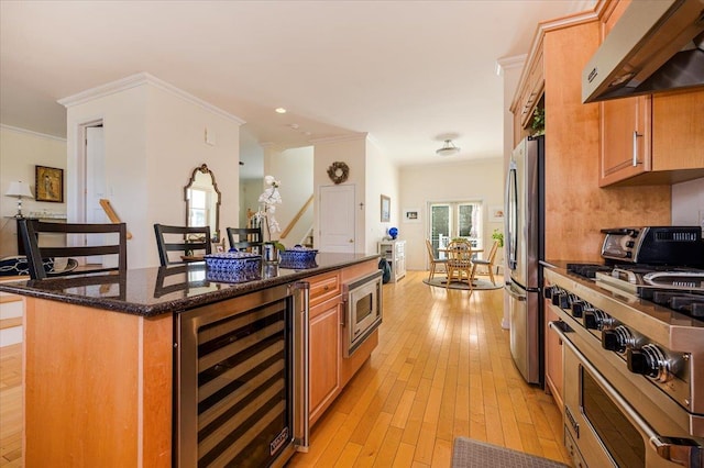 kitchen with beverage cooler, exhaust hood, stainless steel appliances, dark stone counters, and crown molding