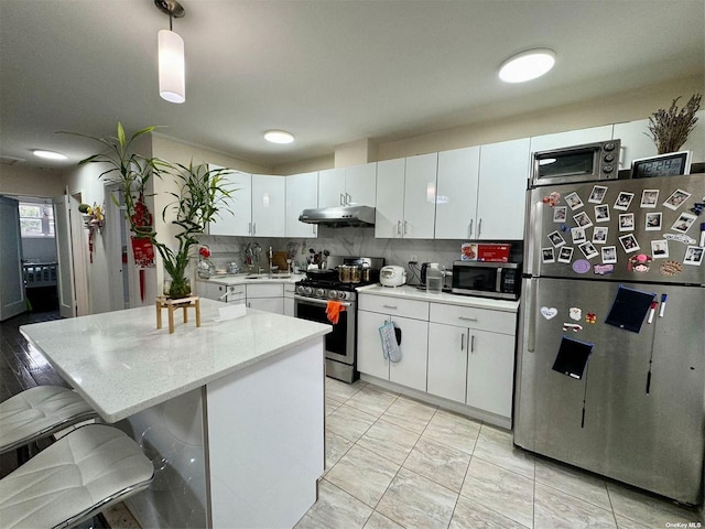 kitchen featuring appliances with stainless steel finishes, hanging light fixtures, white cabinets, and a kitchen bar