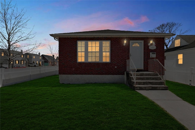 bungalow-style home featuring fence, brick siding, and a lawn