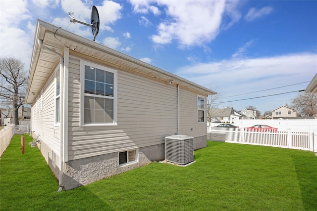 view of side of home with central AC, fence private yard, and a yard