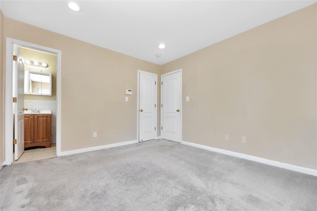 unfurnished bedroom featuring ensuite bath, recessed lighting, baseboards, and light carpet