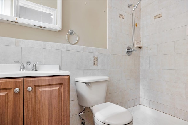 bathroom with a wainscoted wall, toilet, a tile shower, tile walls, and vanity