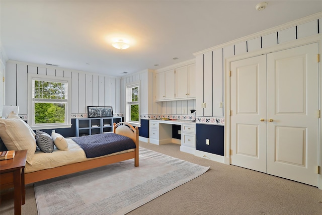 bedroom featuring built in desk, a closet, multiple windows, and light colored carpet