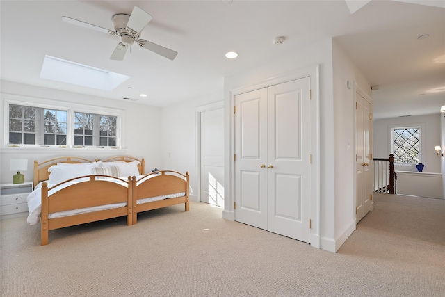 bedroom with a closet, a skylight, light carpet, and ceiling fan