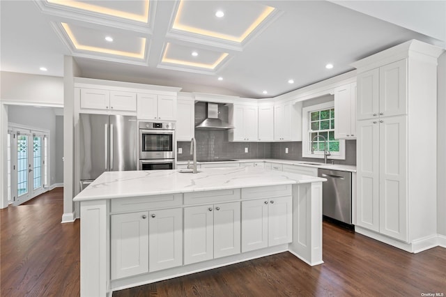 kitchen featuring stainless steel appliances, a kitchen island, wall chimney exhaust hood, sink, and white cabinetry