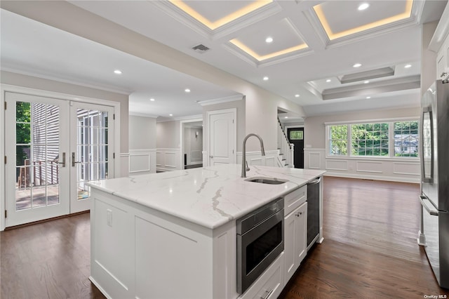 kitchen with light stone counters, stainless steel appliances, a kitchen island with sink, and white cabinetry