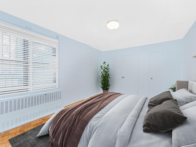 bedroom featuring radiator, multiple windows, and parquet flooring