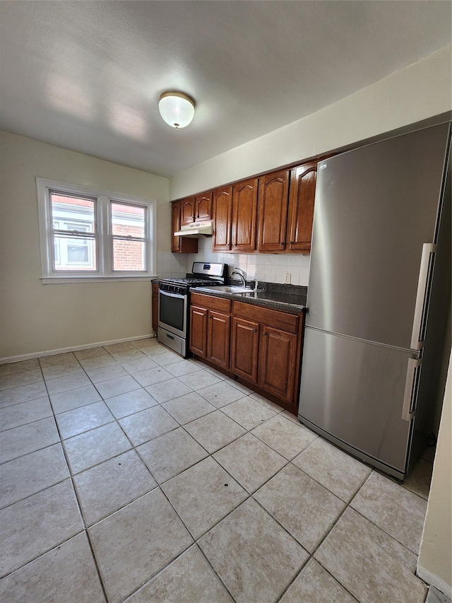 kitchen featuring light tile patterned floors, under cabinet range hood, stainless steel appliances, decorative backsplash, and dark countertops