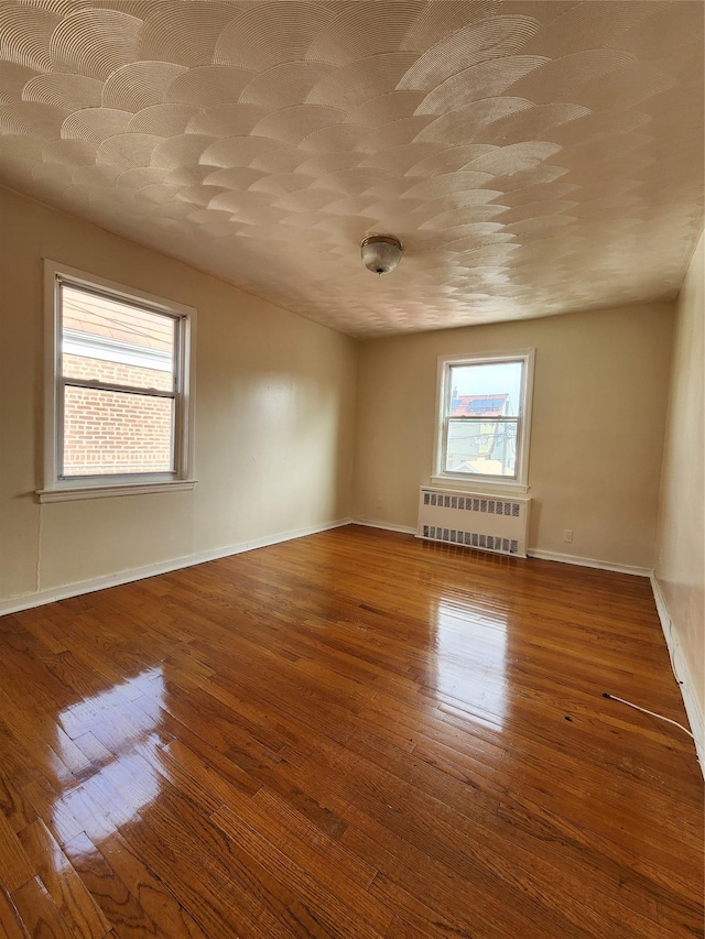 spare room featuring radiator, baseboards, and hardwood / wood-style floors