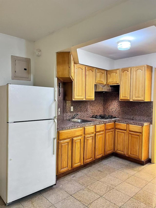 kitchen featuring white fridge, electric panel, stainless steel gas stovetop, backsplash, and sink