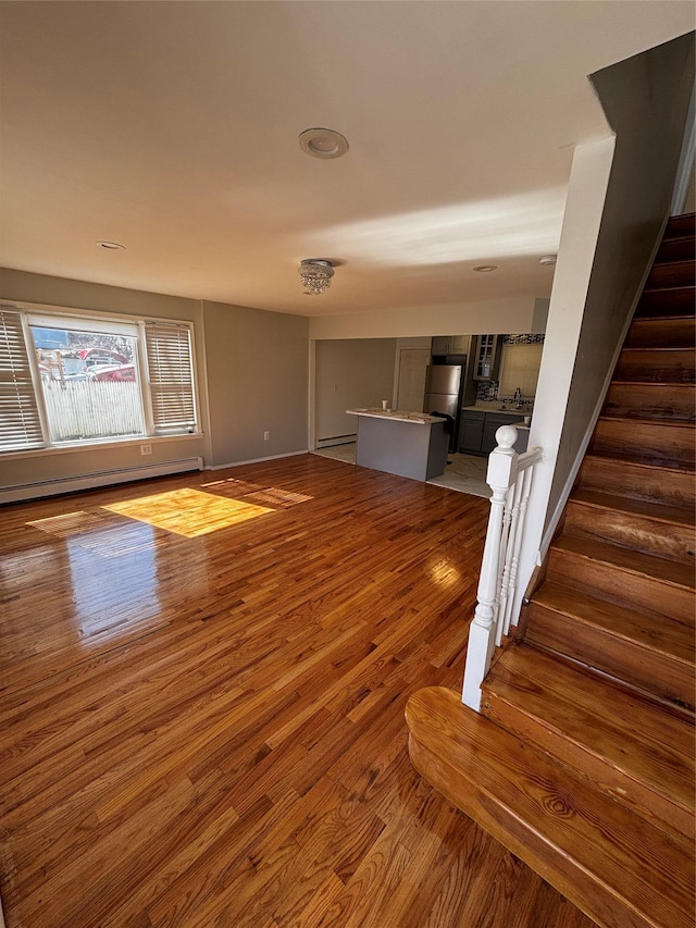 unfurnished living room with a baseboard radiator, stairway, and wood finished floors