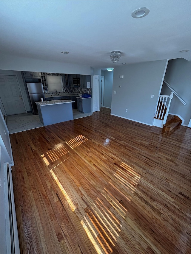 unfurnished living room featuring stairs, baseboard heating, wood finished floors, and baseboards