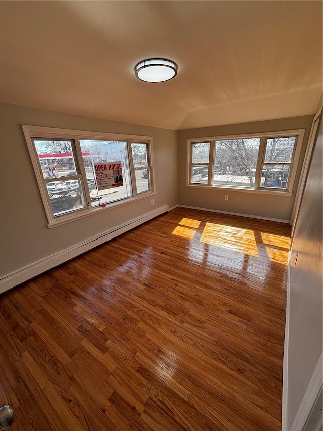 unfurnished room featuring a baseboard heating unit, vaulted ceiling, baseboards, and wood finished floors