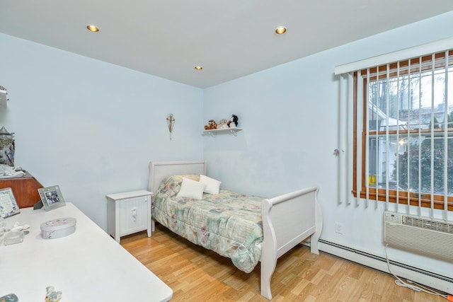 bedroom with baseboard heating, light hardwood / wood-style flooring, and a wall mounted air conditioner