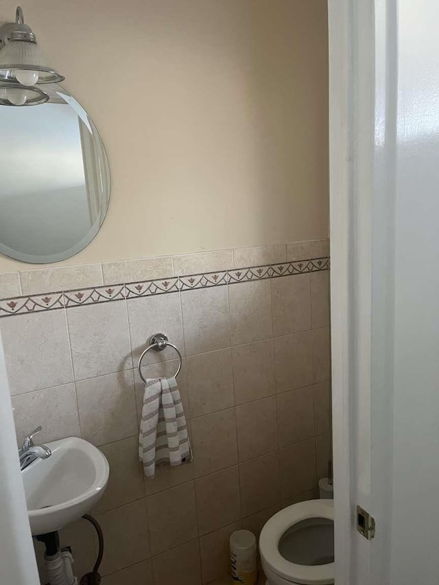 bathroom featuring toilet, sink, and tile walls