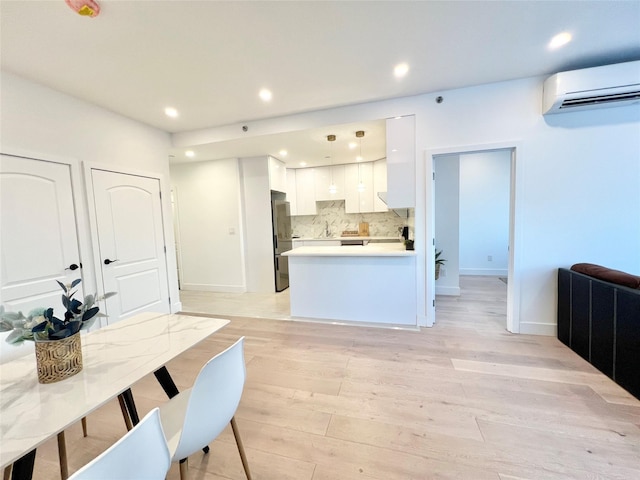 kitchen with white cabinetry, decorative light fixtures, light wood-type flooring, a wall unit AC, and decorative backsplash