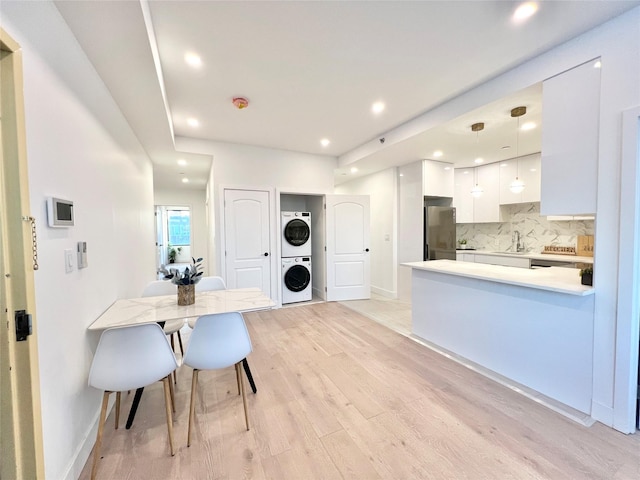 kitchen featuring stacked washer and dryer, stainless steel fridge, decorative backsplash, white cabinets, and decorative light fixtures