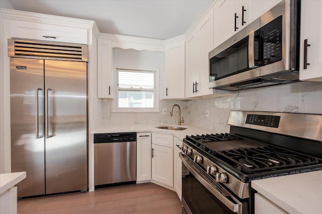 kitchen featuring stainless steel appliances, sink, white cabinets, light wood-type flooring, and tasteful backsplash