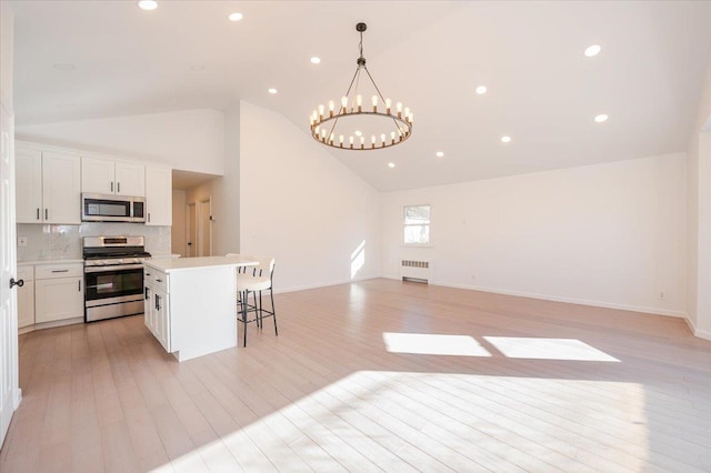 kitchen with stainless steel appliances, white cabinets, decorative light fixtures, radiator, and a kitchen island