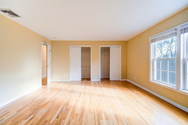 unfurnished bedroom with light wood-type flooring and multiple closets