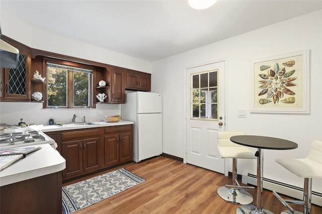 kitchen with sink, white fridge, a baseboard heating unit, dark brown cabinetry, and light hardwood / wood-style flooring