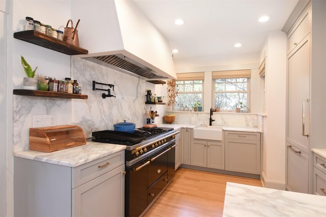 kitchen with range with two ovens, open shelves, tasteful backsplash, a sink, and premium range hood