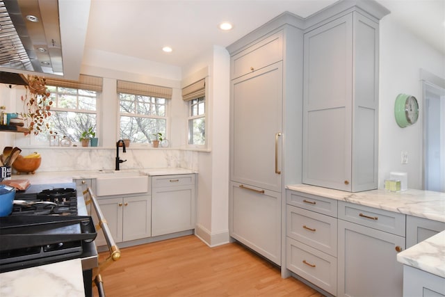 kitchen with recessed lighting, gray cabinetry, a sink, light stone countertops, and light wood-type flooring