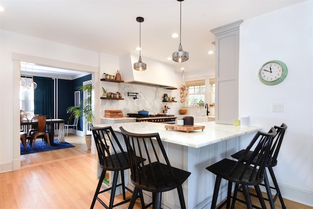 kitchen with a breakfast bar area, stove, light wood-type flooring, open shelves, and tasteful backsplash