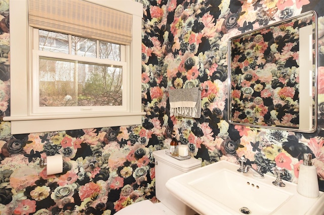 bathroom featuring a sink, toilet, and wallpapered walls