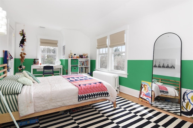 bedroom with radiator, visible vents, and wood finished floors