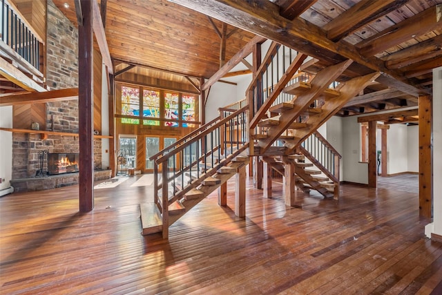 interior space featuring a stone fireplace, wood ceiling, wood-type flooring, a towering ceiling, and beam ceiling