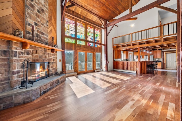 unfurnished living room featuring hardwood / wood-style flooring, vaulted ceiling, a stone fireplace, a baseboard radiator, and wooden ceiling