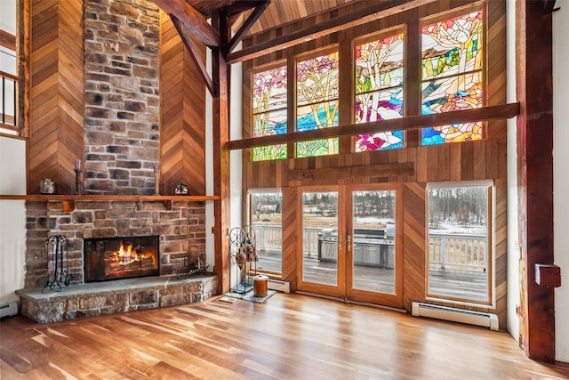 unfurnished living room with a healthy amount of sunlight, wooden walls, a high ceiling, and a baseboard heating unit