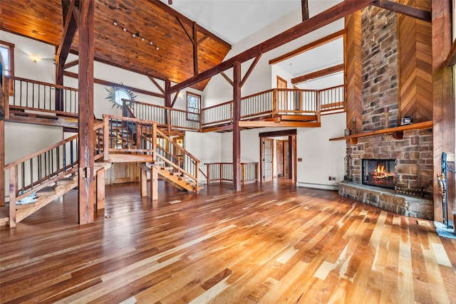 living room with a stone fireplace, wood-type flooring, high vaulted ceiling, beamed ceiling, and a baseboard heating unit