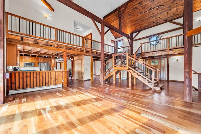 unfurnished living room featuring light hardwood / wood-style flooring, high vaulted ceiling, beamed ceiling, and baseboard heating