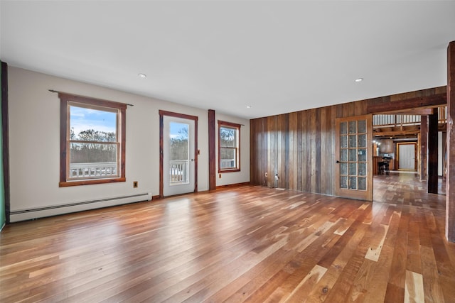 unfurnished living room featuring wood-type flooring, baseboard heating, and wood walls